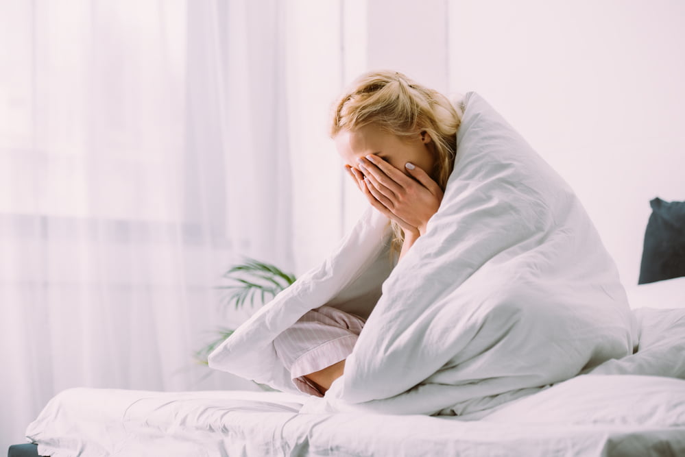Depressed woman crying in bed with blankets over her