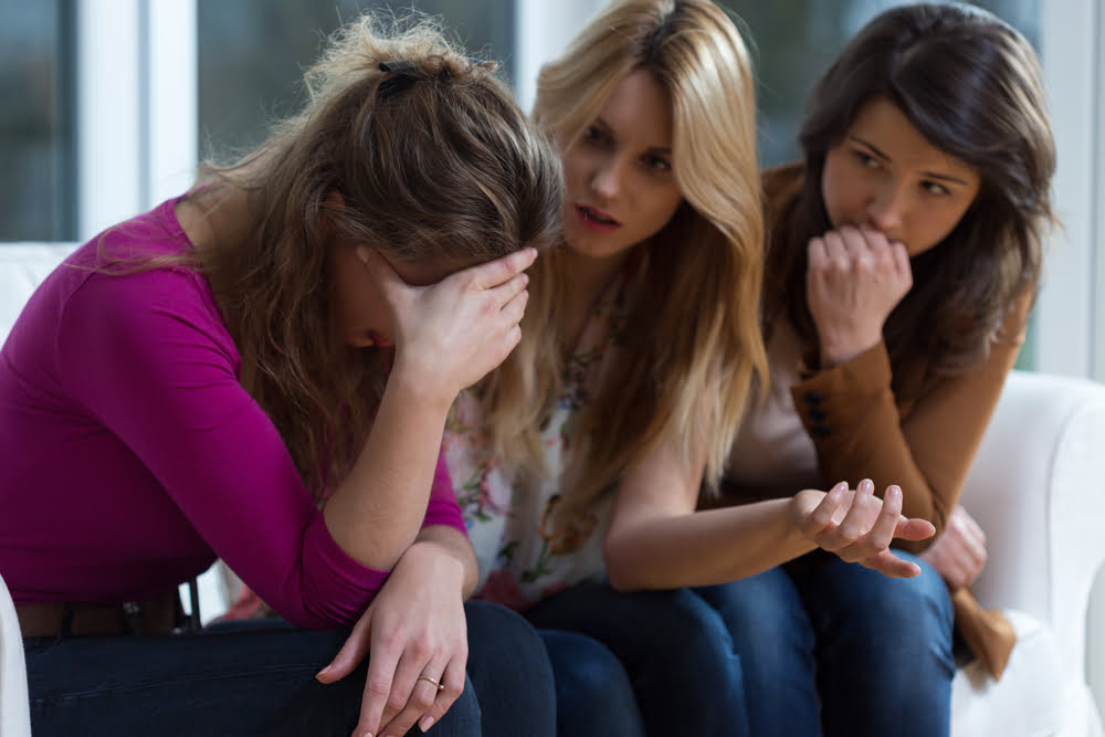 Depressed girl sitting with her friends who are trying to help her