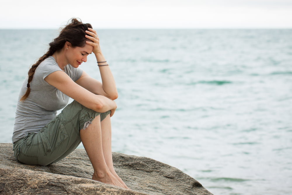 Grieving woman crying by the ocean with her hand on her head